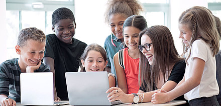 Grundschullehrerin zeigt ihren Schüler:innen begeistert etwas an Laptop