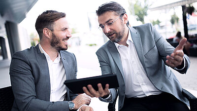 Deux hommes discutent en regardant une tablette