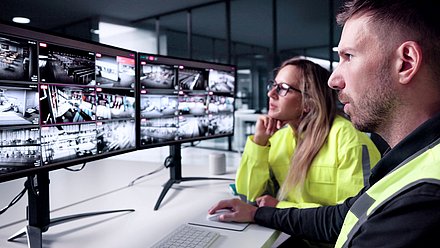 Foto: Zwei Personen sitzen vor mehreren Monitoren mit Kamera-Livebildern und überwachen eine Sicherheits- und Videoüberwachungsanlage.