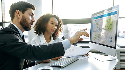 Zwei Mitarbeitende schauen auf einen Monitor, die die LANCOM Management Cloud zeigt