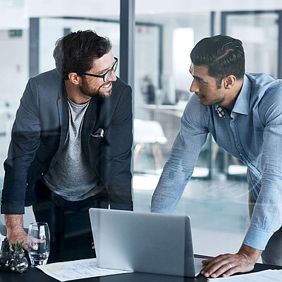 Zwei Verwaltungsmitarbeiter unterhalten sich an Laptop in Büro angeregt über die digitale Souveränität ihrer Firma