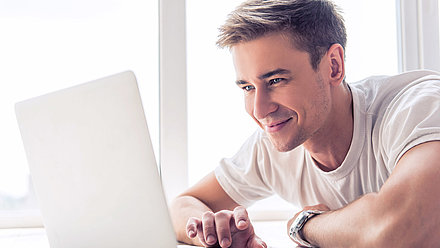 Glücklich-entspannter junger Mann beobachtet erfreut die Auswirkungen seines optimierten WLANs auf seinem Laptop
