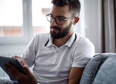 Zufriedener Bürger erledigt seine Verwaltungsangelegenheiten entspannt über sein Tablet von seinem Sofa aus