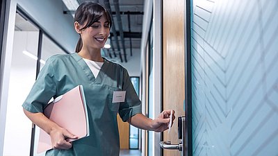 Foto: Mitarbeiterin im Gesundheitswesen öffnet mit einer Zutrittskarte eine gesicherte Tür und steht beispielhaft für digitale Zugriffsrechte und moderne Zugangskontrolle in sensiblen KRITIS-Bereichen.