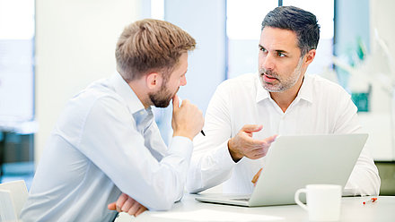 Zwei Büroarbeiter unterhalten sich ernst vor Laptop in Büro