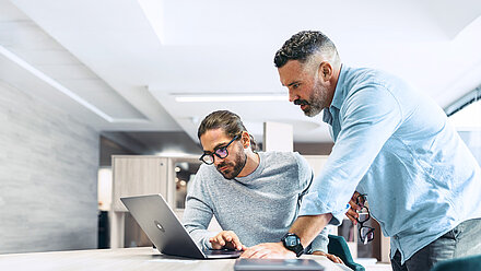 Männer lehnen sich über einen Laptop.