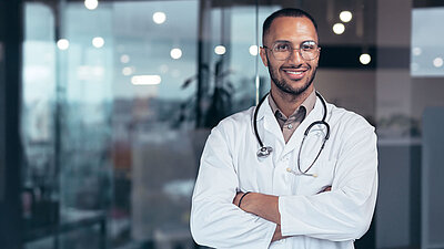 Mann im Arztkittel und mit verschränkten Armen lächelt in die Kamera