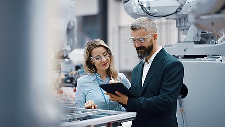 Zwei Personen stehen mit einer Schutzbrille in einem Labor an einem Tablet