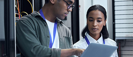 Männlicher und weiblicher IT-Administrator beraten sich in Serverraum an Laptop zu besserem Netzwerkmanagement
