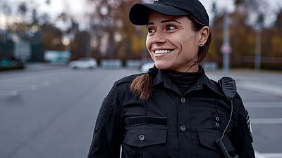 Foto: Sicherheitsmitarbeiterin in schwarzer Uniform mit Funkgerät überwacht aufmerksam einen Außenbereich und steht beispielhaft für sichere Überwachungs- und Schutzkonzepte in kritischen Infrastrukturen.