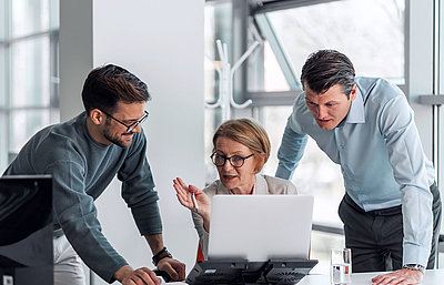 Gruppe von drei Verwaltungsmitarbeitenden sitzt in Büro an Laptop und berät sich