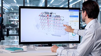 Foto: Person sitzt vor großem Monitor mit digitalem Gebäude- und Netzwerkmodell und bedient die Darstellung per Touch-Geste.