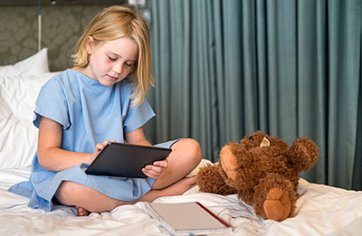 Kleines Mädchen sieht sich im Krankenbett mit ihrem Teddy Film auf Tablet an