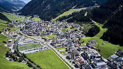 Foto der Gemeinde Ischgl von oben aus dem Flugzeug aufgenommen: Idyllische Häuser und Straßen im Tal zwischen den Bergen