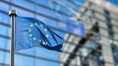 Bild von EU-Flagge von sich in Fensterfront spiegelndem Gebäude