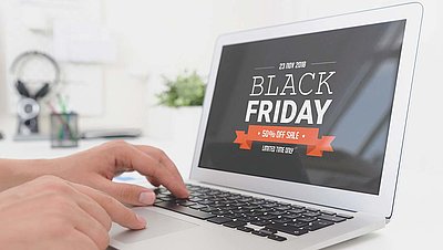 Laptop mit Black Friday Sale Angebot auf Bildschirm und zwei Händen, die auf der Tastatur tippen