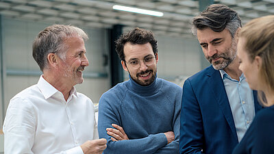 Vier Geschäftsleute im Gespräch, lächelnd und konzentriert in moderner technischer Umgebung.