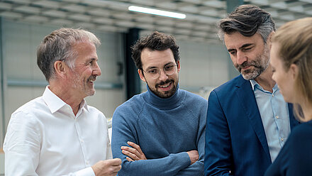 Vier Geschäftsleute im Gespräch, lächelnd und konzentriert in moderner technischer Umgebung.