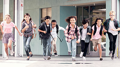 Gruppe von Grundschulkindern rennt fröhlich mit ihren Schultaschen auf den Pausenhof