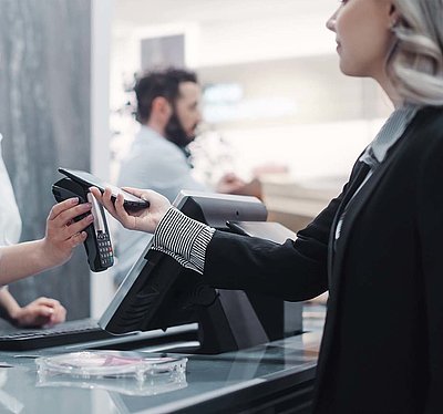 Blonde Kundin in schwarzem Blazer bezahlt kontaktlos mit ihrem Smartphone an der Kasse eines modernen Geschäfts