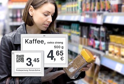 Brünette Frau betrachtet Instant-Kaffee aus Shop-in-Shop-Kaffeeregal mit elektronischen Preisschildern im Supermarkt mit vergrößerter Darstellung zweier Displays in der unteren linken Bildecke