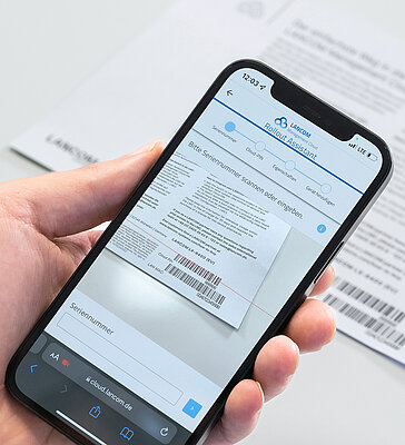 Hand hält Smartphone und scannt damit Barcode vom LANCOM cloud-ready Beileger ein