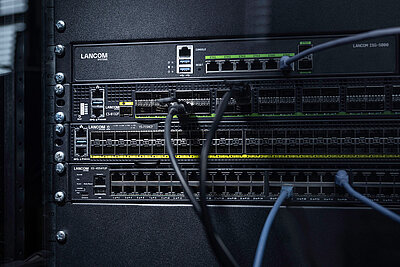 Drei LANCOM Switches eingebaut im Rack mit Kabeln: Core Switch LANCOM CS-8132F, Aggregation Switch LANCOM YS-7154CF und Access Switch LANCOM XS-4554XUP