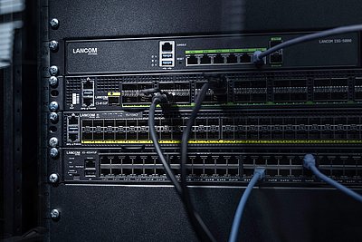 Drei LANCOM Switches eingebaut im Rack mit Kabeln: Core Switch LANCOM CS-8132F, Aggregation Switch LANCOM YS-7154CF und Access Switch LANCOM XS-4554XUP