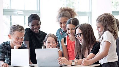Grundschullehrerin zeigt ihren Schüler:innen begeistert etwas an Laptop