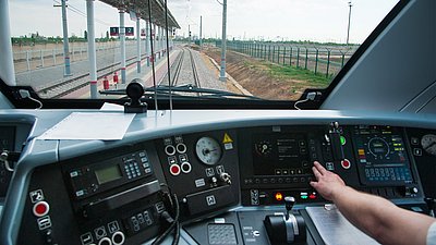 Foto: Blick aus dem Führerstand eines Zuges auf Bahngleise und Bahnsteig; im Vordergrund befinden sich Bedienelemente und Displays.