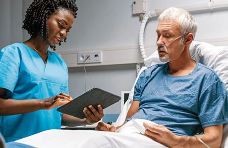 Ärztin steht mit digitalen Patientendokumenten an Krankenbett von Patient