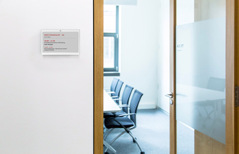 Leerer Meetingraum mit offener Tür, der mit einem LANCOM Wireless ePaper Display beschildert ist